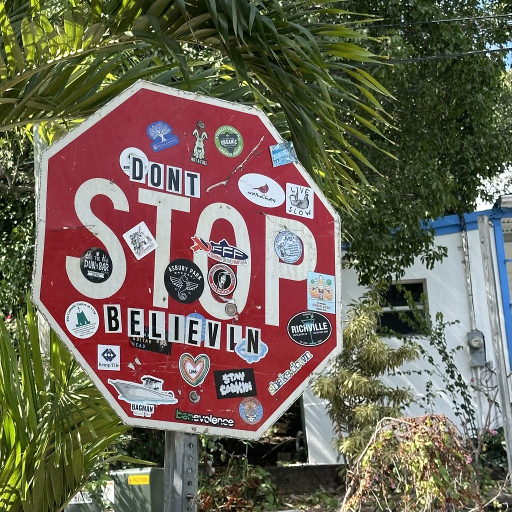 Photograph of a stop sign in Cruz Bay, St. John. It has many stickers added, including letters that make it read "Don't Stop Believin"